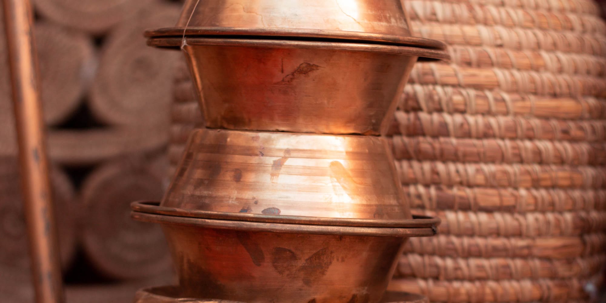 Hammered copper vessels stacked one inside another beside a woven grain basket