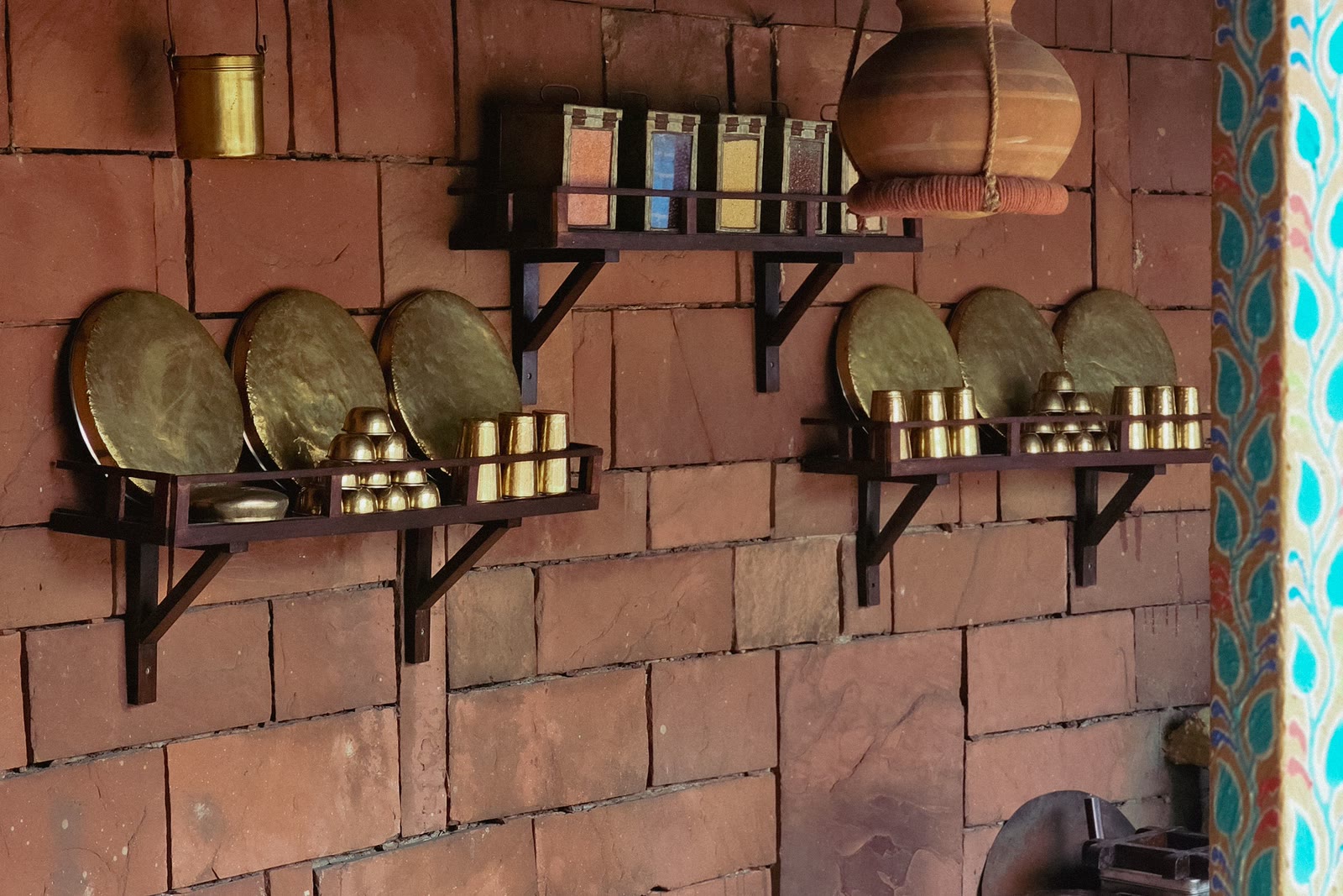 Brass thalis and stacked vessels on iron brackets against the brick wall of a traditional kitchen