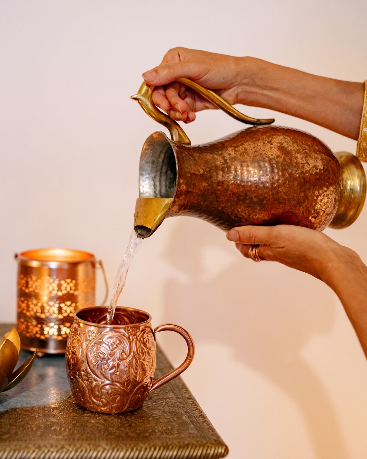 Water being poured from a hammered copper jug into an engraved copper tumbler
